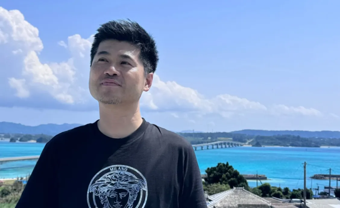 南国の綺麗な海をバックに立っている代表の写真。